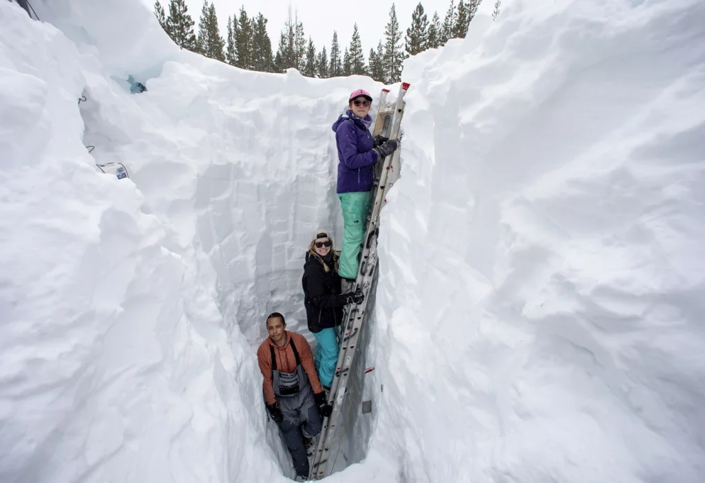 Three researchers stand along a ladder in a nearly 18 foot deep snow pit 