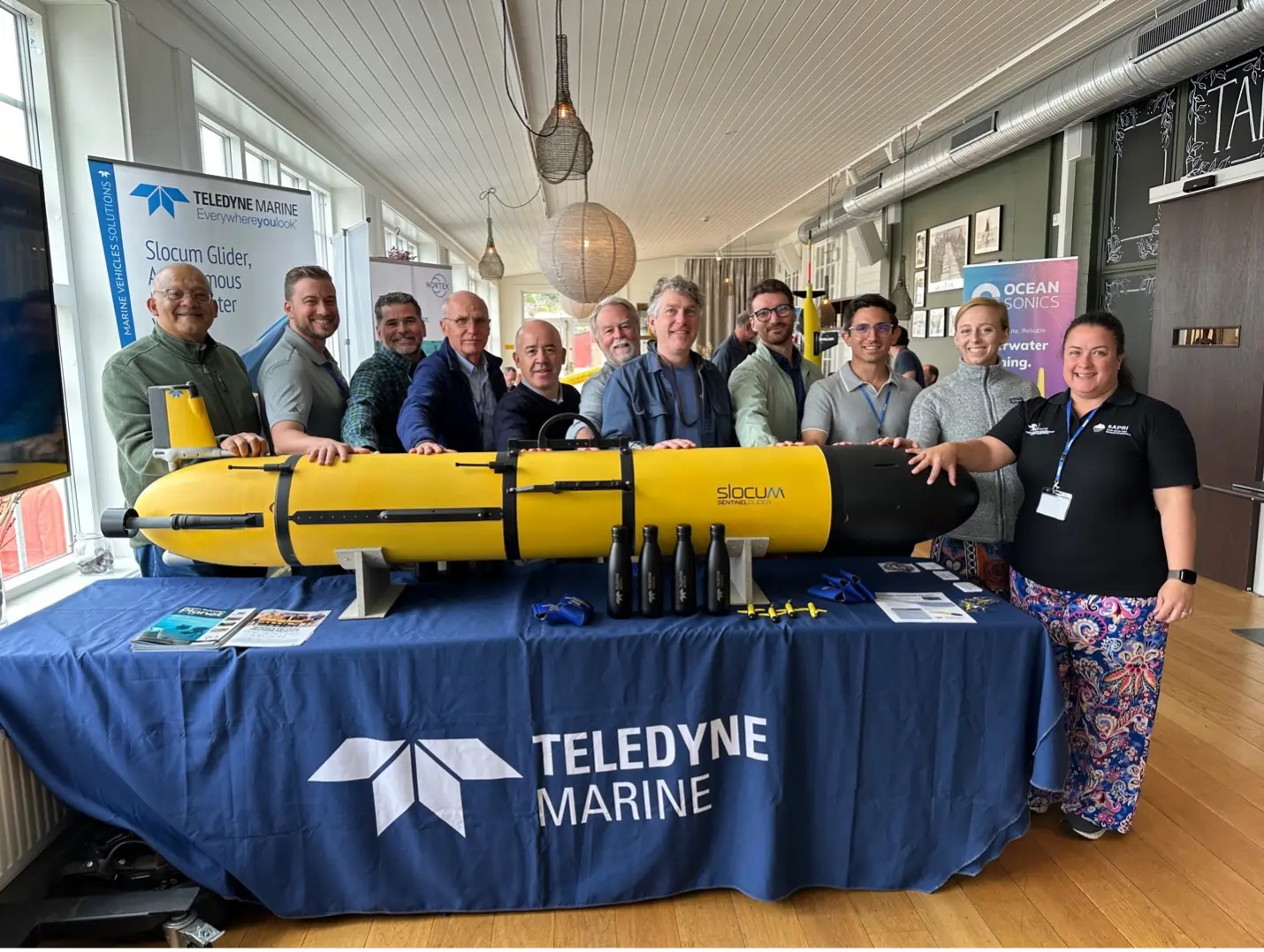 Model of Teledyne Webb Research's new Sentinel Glider along with members of the team of scientists and engineers assisting with piloting this vehicle around the world.