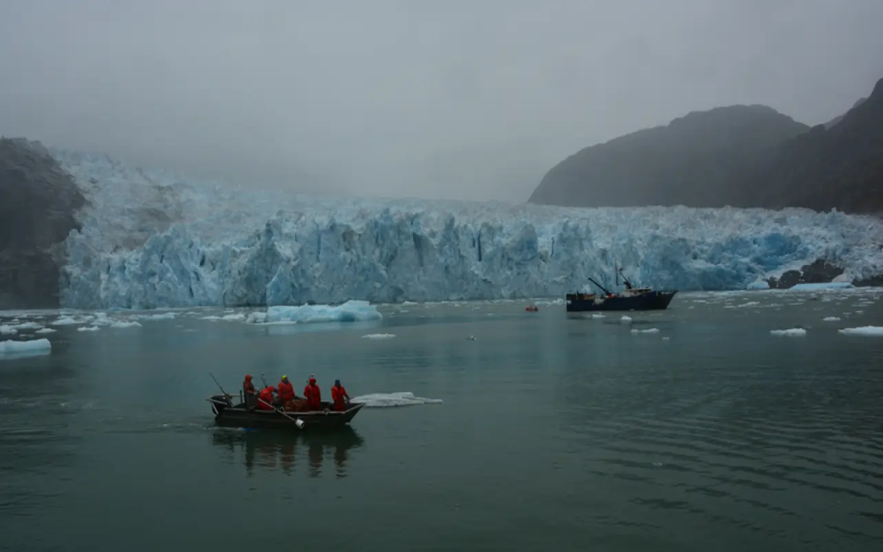 Small boat surveying with one of the larger ships and the glacier in the background.