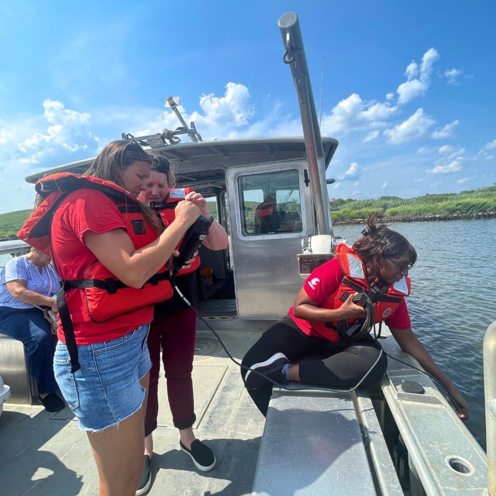 Two participants learn to how scientists take samples of the Raritan River, assisted by Dr. Carrie Ferraro.