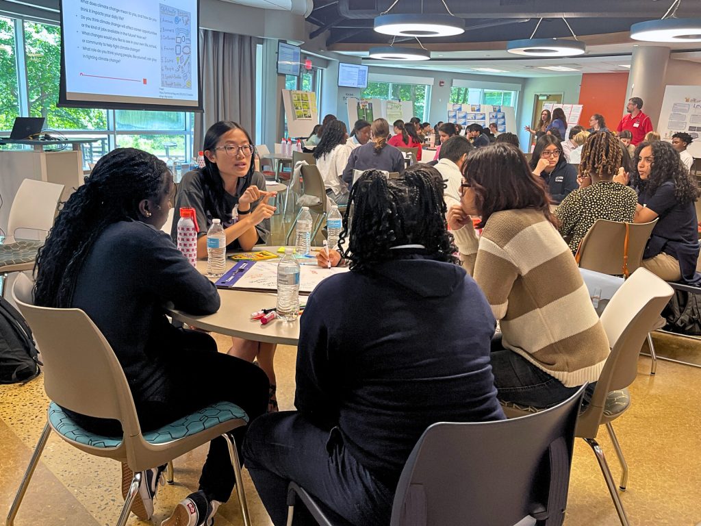 A group of students at the Climate Teen Summit sitting around a table and holding a discussion. 