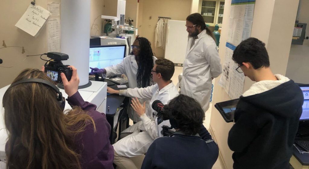 Or Doni filming scientists gathered around and pointing at a computer in a lab