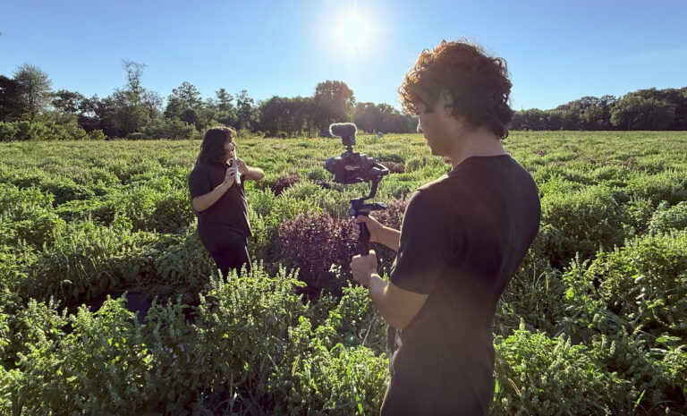 Colby Koutrakos filming a woman playing the flute in a field