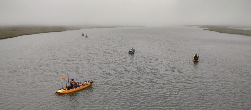 Kayak anglers kayaking down a large body of water with marshes on each side