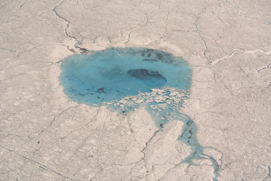 A blue pool of water in the middle of the white Greenland ice sheet