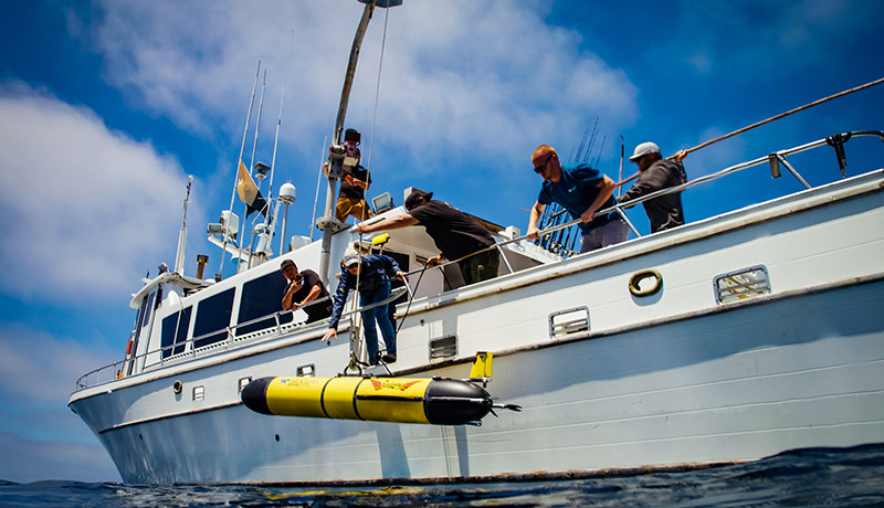 Marine scientists lowering the Redwing vehicle off of a boat into the ocean for testing