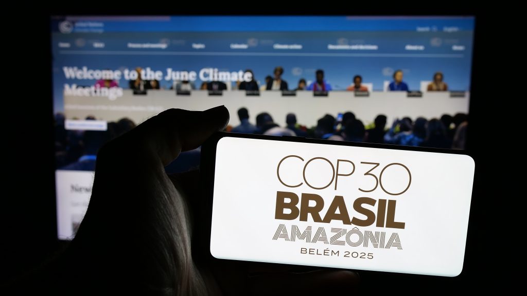 Person holding mobile phone with the logo of the UN climate change conference, COP30 in Brazil, on its screen, in front of web page that reads "Welcome to the June Climate Meetings".