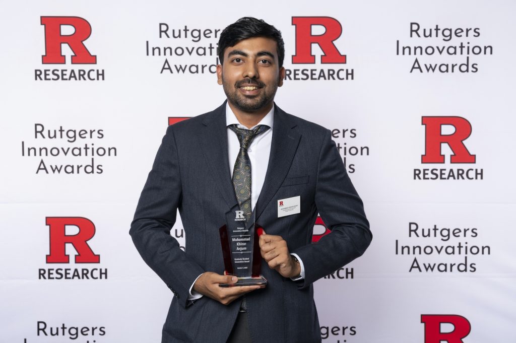 Khizar Anjum holding a trophy in front of a background that reads "Rutgers Innovation Awards" 