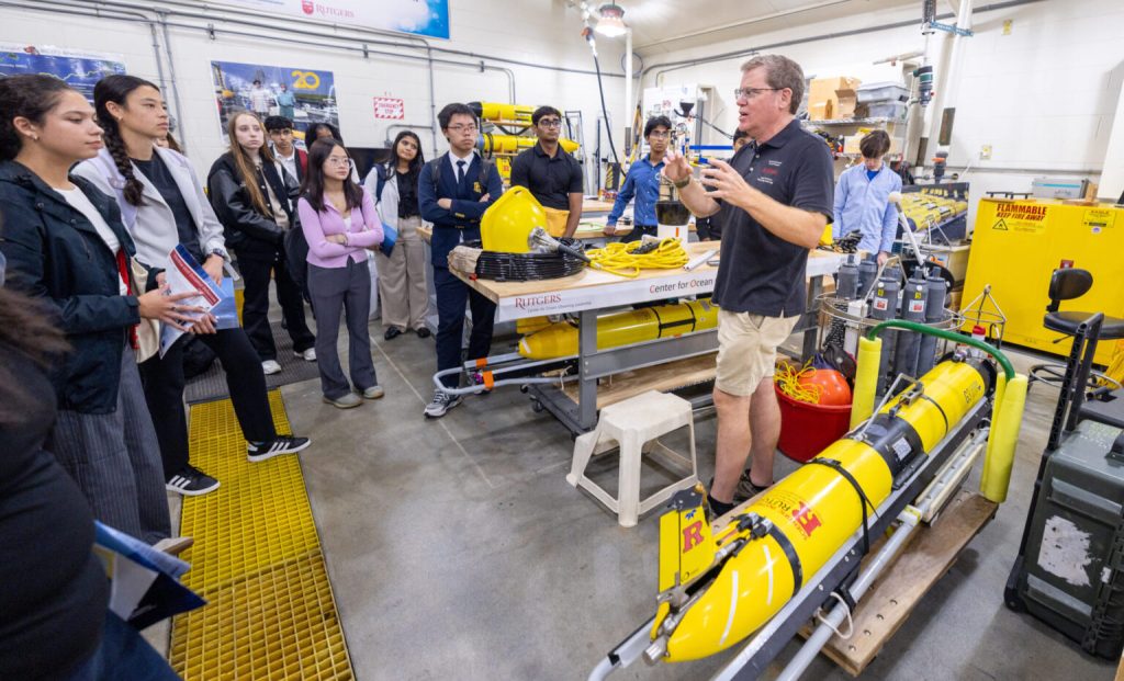 Michael Crowley stands in his lab showing ocean glider prototypes to a group of listening students