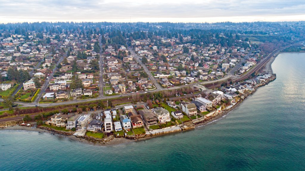 Aerial view of a suburban town on the edge of the water, ocean and shoreline at the front, while the town extends onward into the horizon