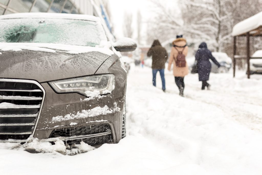 Car parked in snowdrift at city street. Heavy winter snowfall with people walking in strong snow and  wind, blizzard conditions.