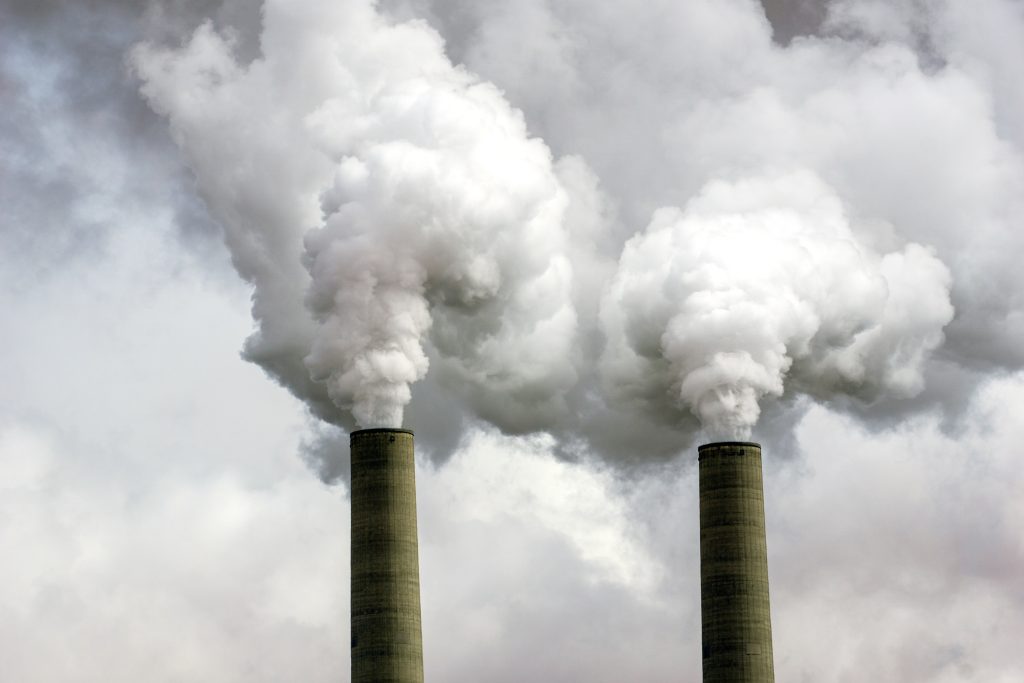 Two smoke stacks emitting dense clouds into a gray sky