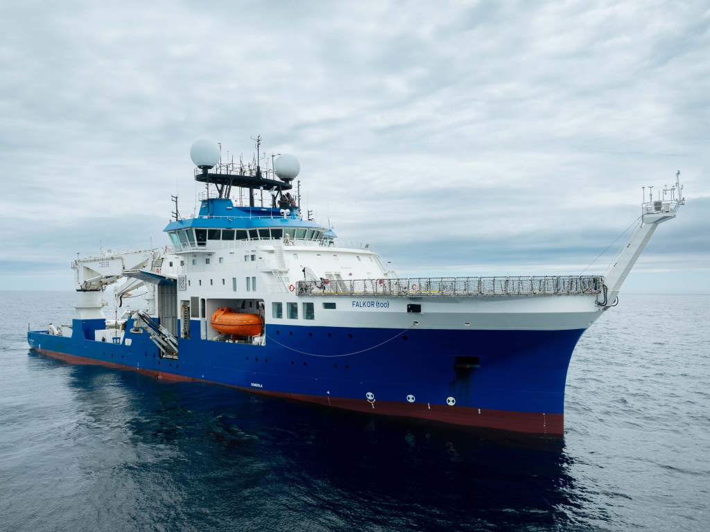 Full side view of a massive boat labelled "FALKOR" on the side as it sails on the ocean