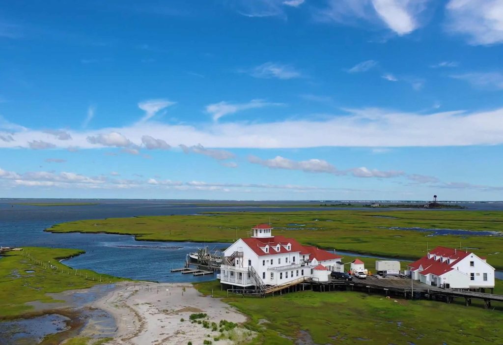 An aerial view of the Rutgers Marine Field Station's buildings, sitting on top of and surrounded by water and marshland on a clear day.