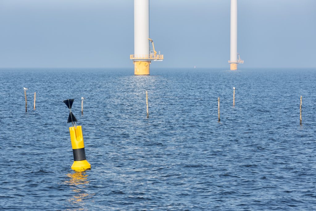 Sunny day on the sea with the poles of offshore wind turbines near Dutch coast with buoy and poles for fishing nets