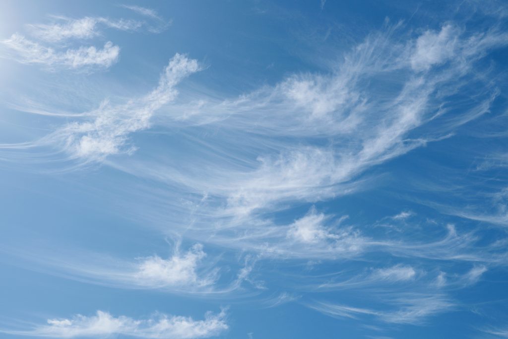 Wispy cirrus clouds, swirling like they are pushed by the wind, in blue sky on sunny day