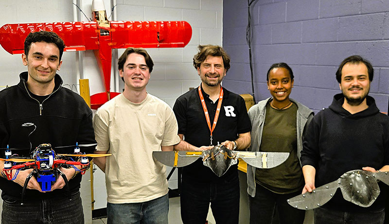 Professor Onur Bilgen standing in the middle of a group of students. They hold models of bird-like robots with large wings.