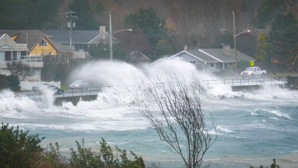 Waves washing onto the road, houses and cars in the background