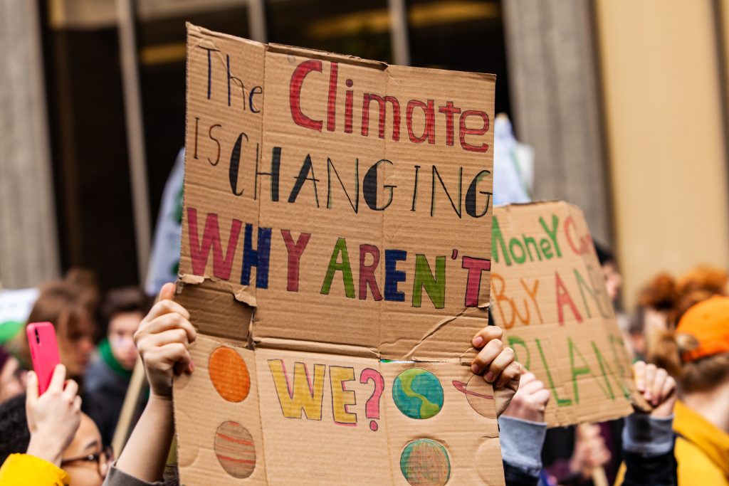 A colorful cardboard placard is viewed close up, saying "The climate is changing, why aren't we?" in the hands of ecological activists as they protest in the city