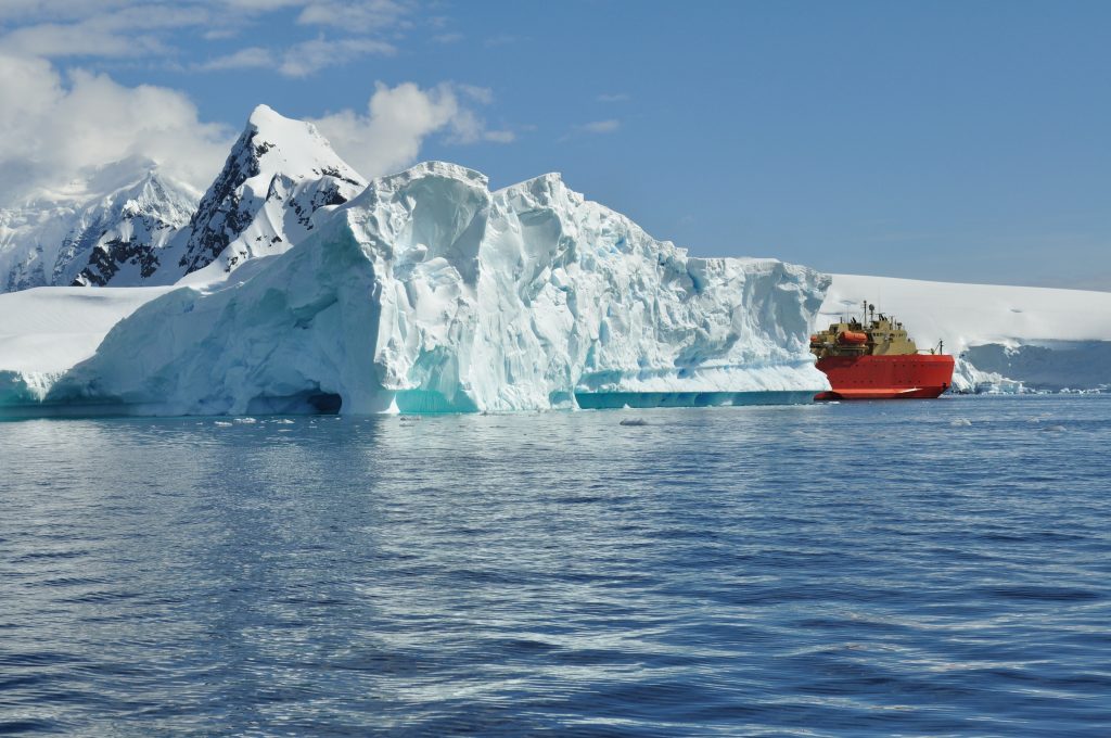 The large boat, a research vessel, pokes its nose out between two glaciers as it traverses the Antarctic waters