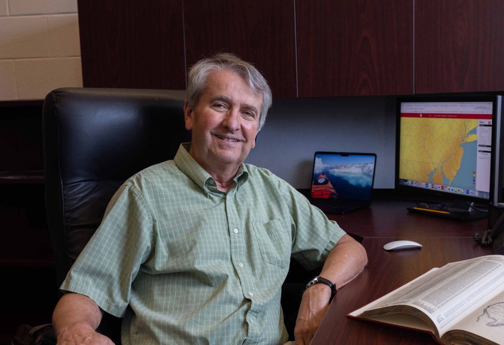 David Robinson sits smiling at his desk with his computer open to a map of New Jersey in the background.