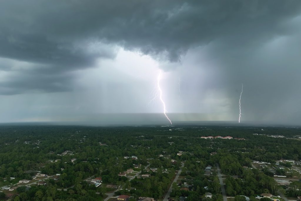 Dark stormy clouds and lightning forming on gloomy sky before heavy rainfall over suburban town area.