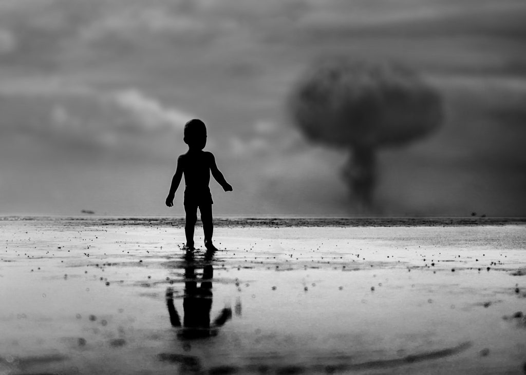 A child standing on the shore in shadow, watching the plume from a nuclear attack in the distance 