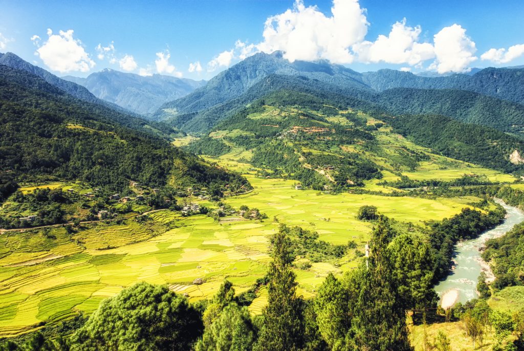 Aerial view of the glacially fed Paro Chhu (Paro River) flowing past rolling hills, trees, and green fields in Bhutan.