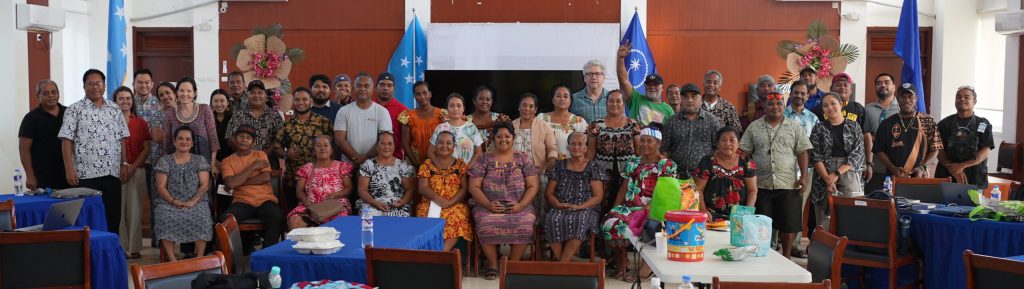 The stakeholders and Rutgers researchers gather for a large group photo in an official room with Kosrae flags hanging in the backgroun.