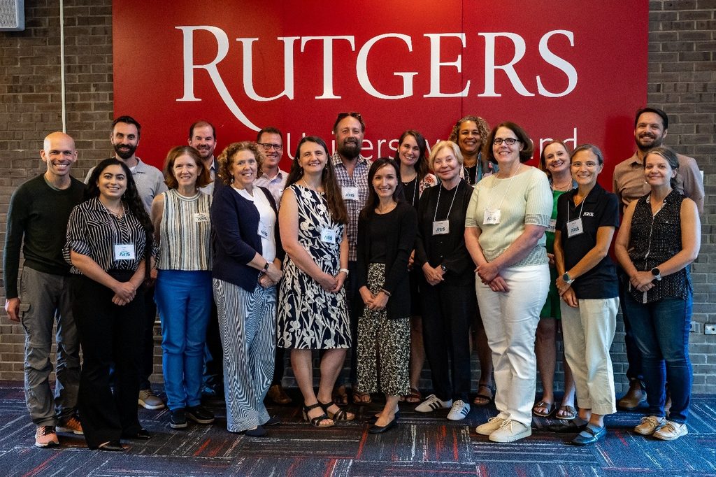 Participants in the Kickoff Welcome Event stand together for a photo in front of a large "Rutgers" sign.