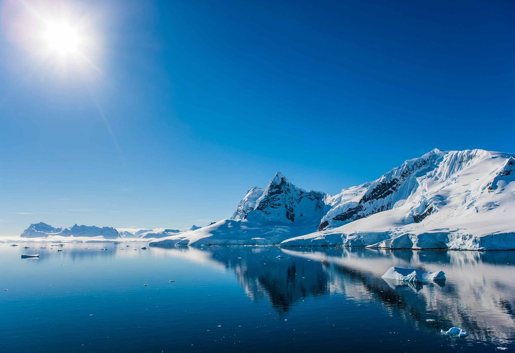 A picturesque view of the the Antarctic landscape, with snow capped glaciers floating in crystal clear waters on a sunny day.