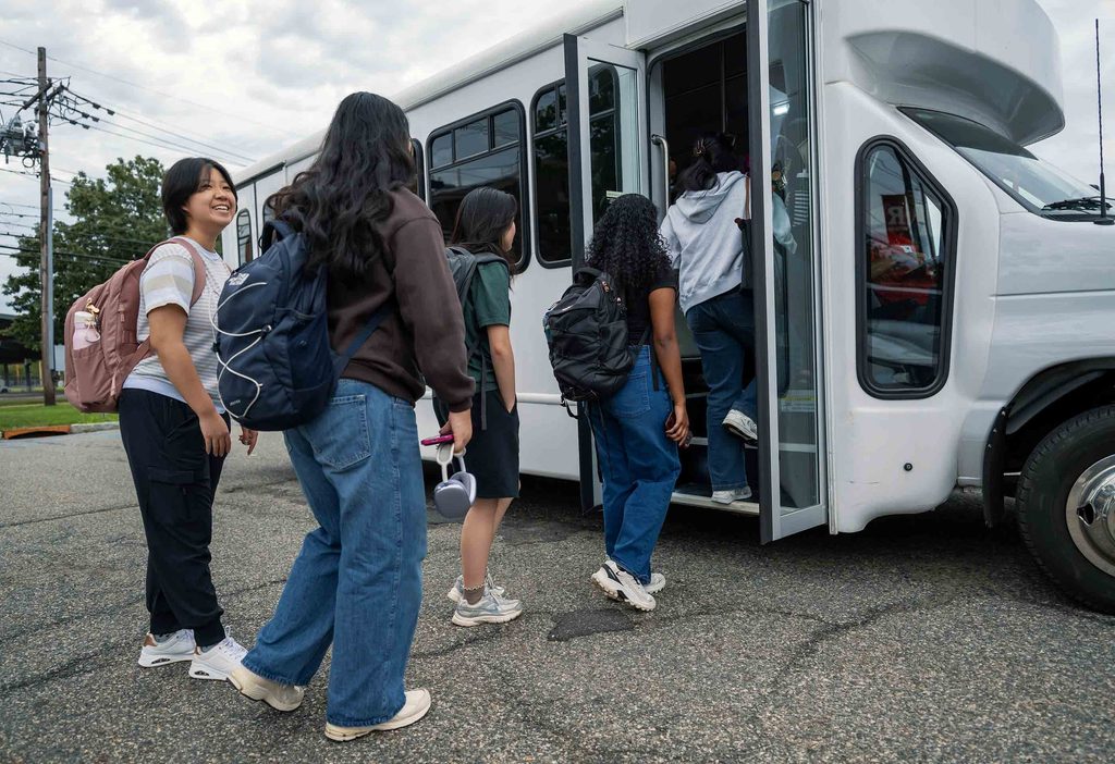 A group of students with backpacks line up to step into a shuttle bus.